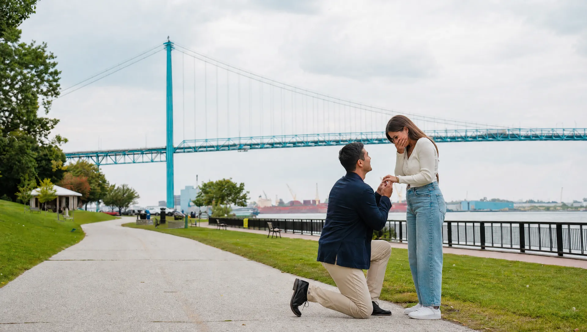 A proposal on the Windsor riverfront with the Ambassador Bridge behind, as he offers her an engagement ring